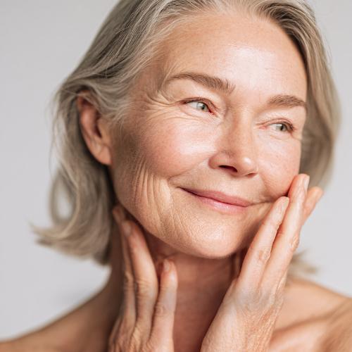 A silver-haired woman smiling gently with her hands resting against her cheeks.
