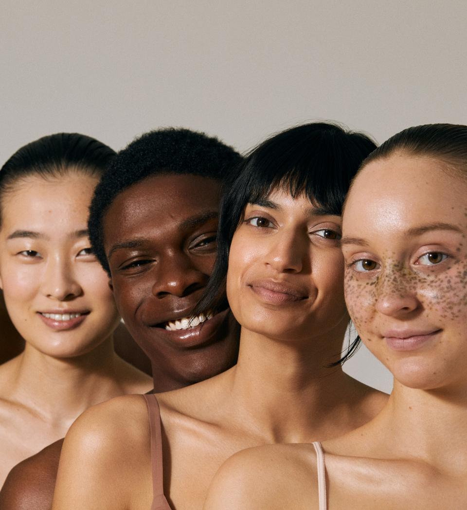 Four people smiling together, with varied complexions, hairstyles and freckles.